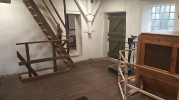 Back room of the top floor of the Mill. The wooden separator for separating different types of flour is on the right. A wooden ladder leads upstairs to the left and another ladder next to it leads to the floor below. 