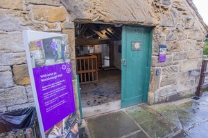 Entrance to the Mill through an open green door with a sign saying 'Welcome to Worsbrough Mill' to the left