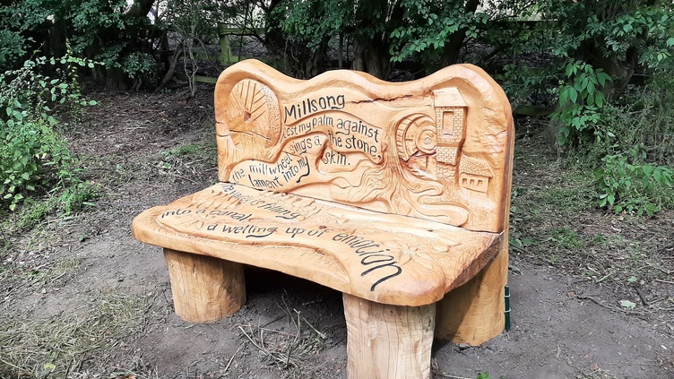 Carved wooden bench with mill items such as millstones and water wheel and words from Eloise's poem