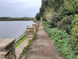 A path along the right hand side of the reservoir with trees and bushes to the right